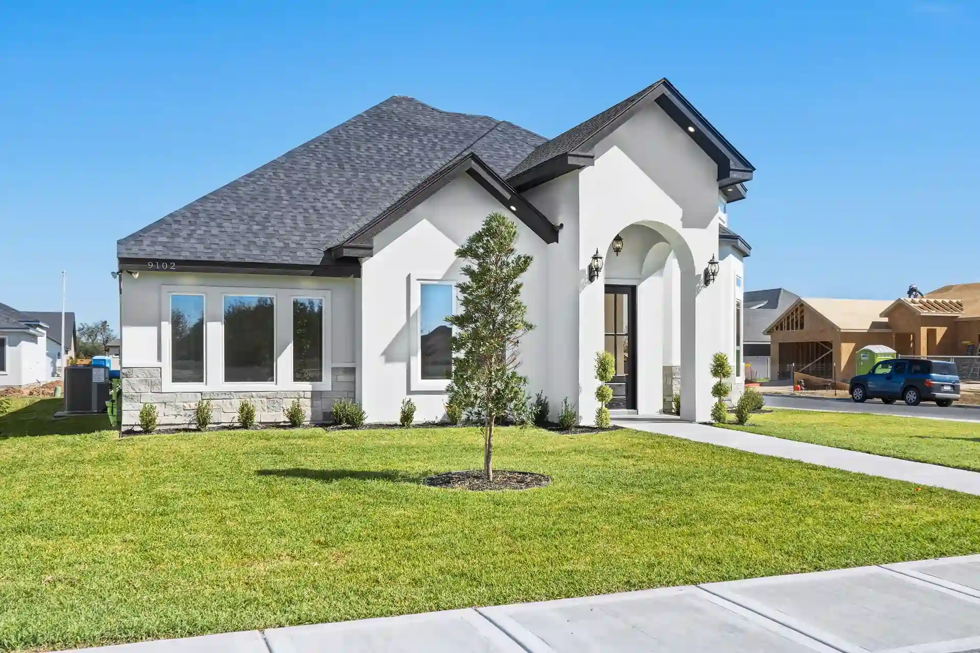 Front exterior of the 9102 N. 25th custom home — white stucco facade, dark hip roof, French entry doors, landscaped lawn